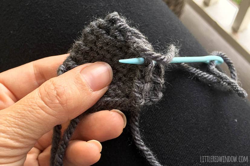 Two knit bear ears getting sewn together with a yarn needle