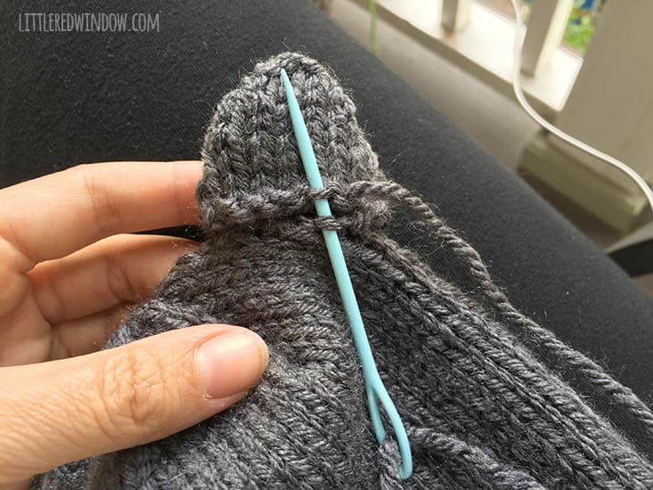hand sewing dark gray knit bear ears onto a hat with a blue yarn needle