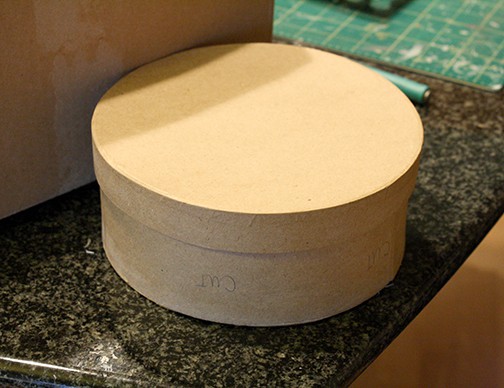 Round paper mache cardboard box with lid on a counter