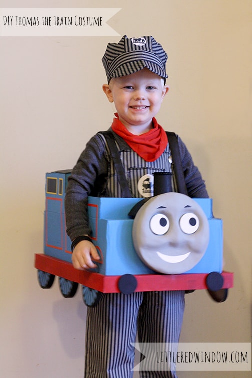 Smiling little boy wearing a train engineer costume and wearing the cardboard Thomas the Train costume!