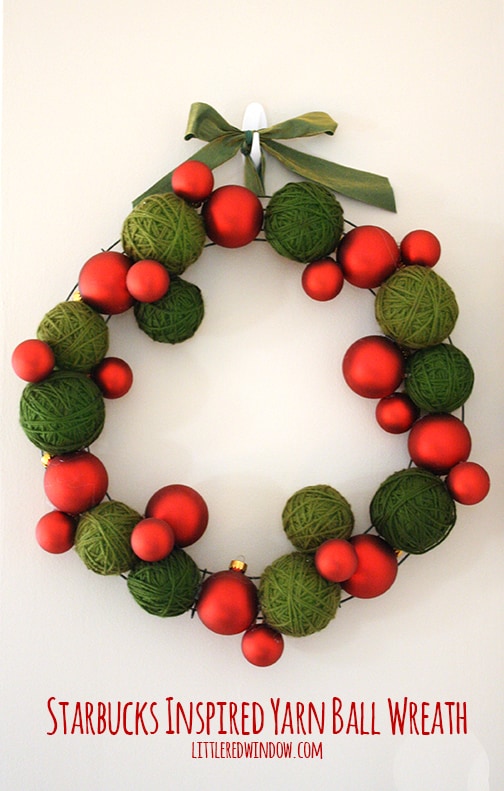 Wreath made of green yarn balls and red Christmas ornaments hanging on a wall
