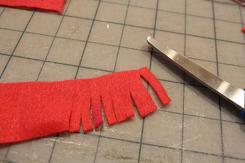 A 2 inch wide strip of hot pink felt on a gray cutting mat cut with fringe along one edge