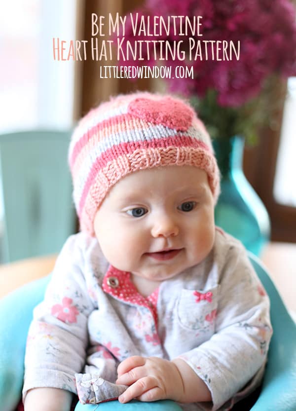 Chubby baby wearing pink striped hat with a heart on the front sitting in a seat