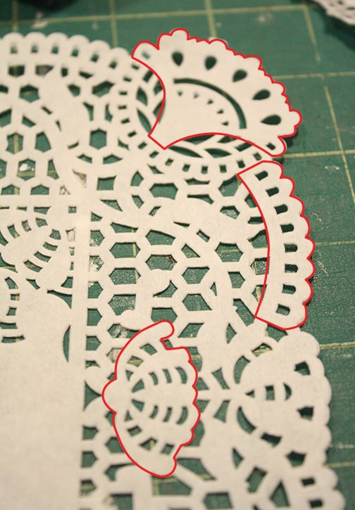 Closeup of paper lace doily with red lines drawn on top to show which sections to cut out