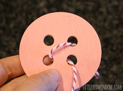 Sewing Room Giant Button Garland Hand holding pink button with twine through the bottom right buttonhole| littleredwindow.com | Make a sweet hand-painted giant button garland for your sewing or craft room with this great tutorial!