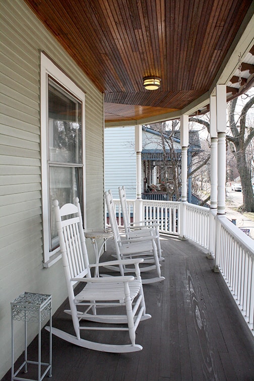 view of a porch with three white rocking chairs on it