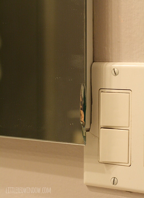 Closup of broken mirror corner and light switch