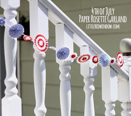 Red and white rosettes strung on baker's twine and hanging along a white railing outside