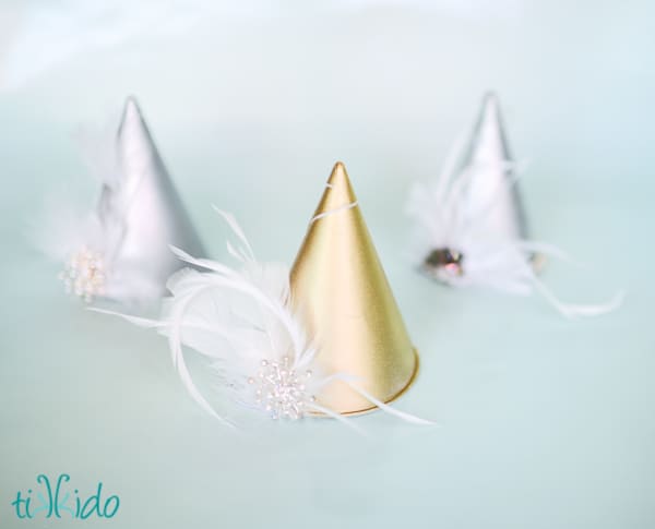 gold and silver party hats with white feathers and brooches on them