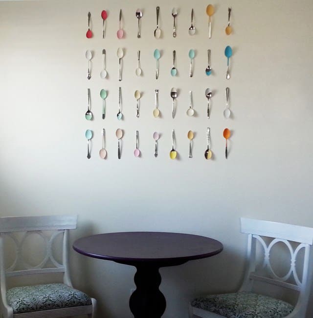 Kitchen wall with a grid of spoons hanging on it. Each spoon has been dipped in a rainbow color