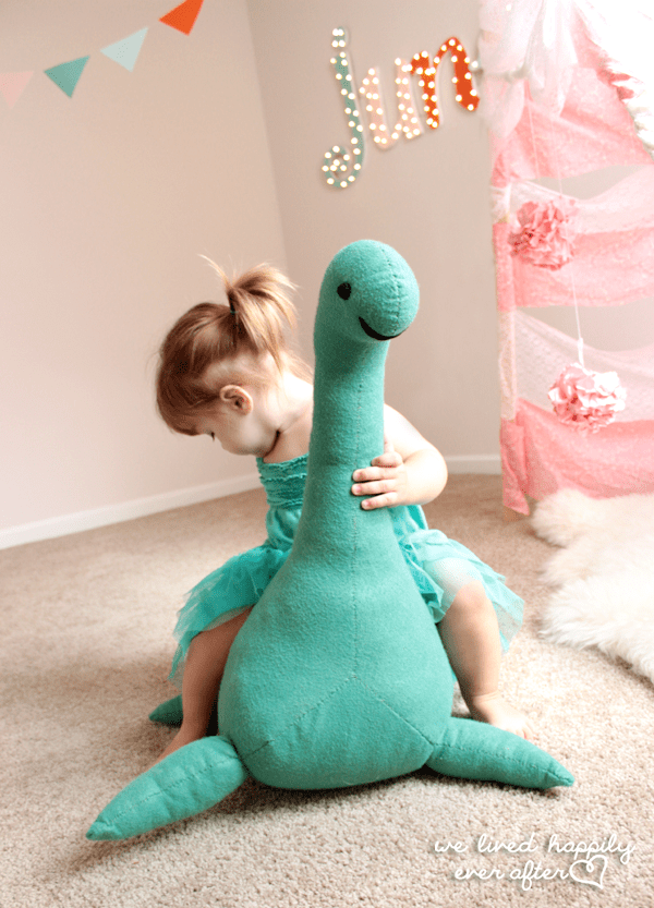 little girl sitting on the back of large teal stuffed loch ness monster