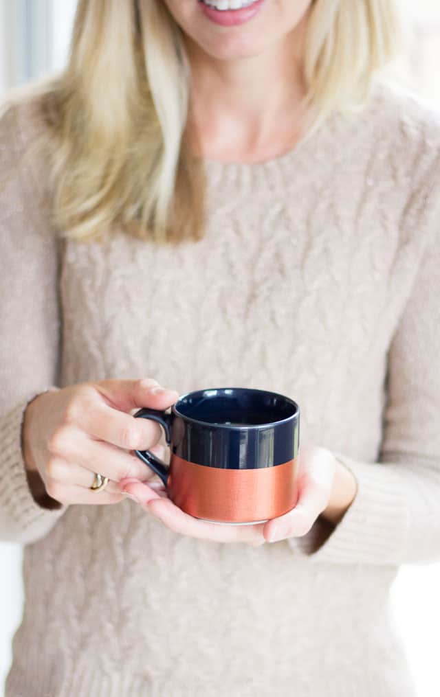 Woman intan sweater holding black mug half painted copper