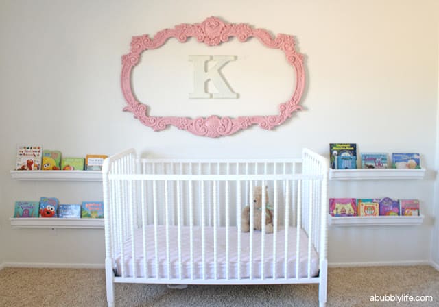 White crib with ornate pink frame and the letter K inside