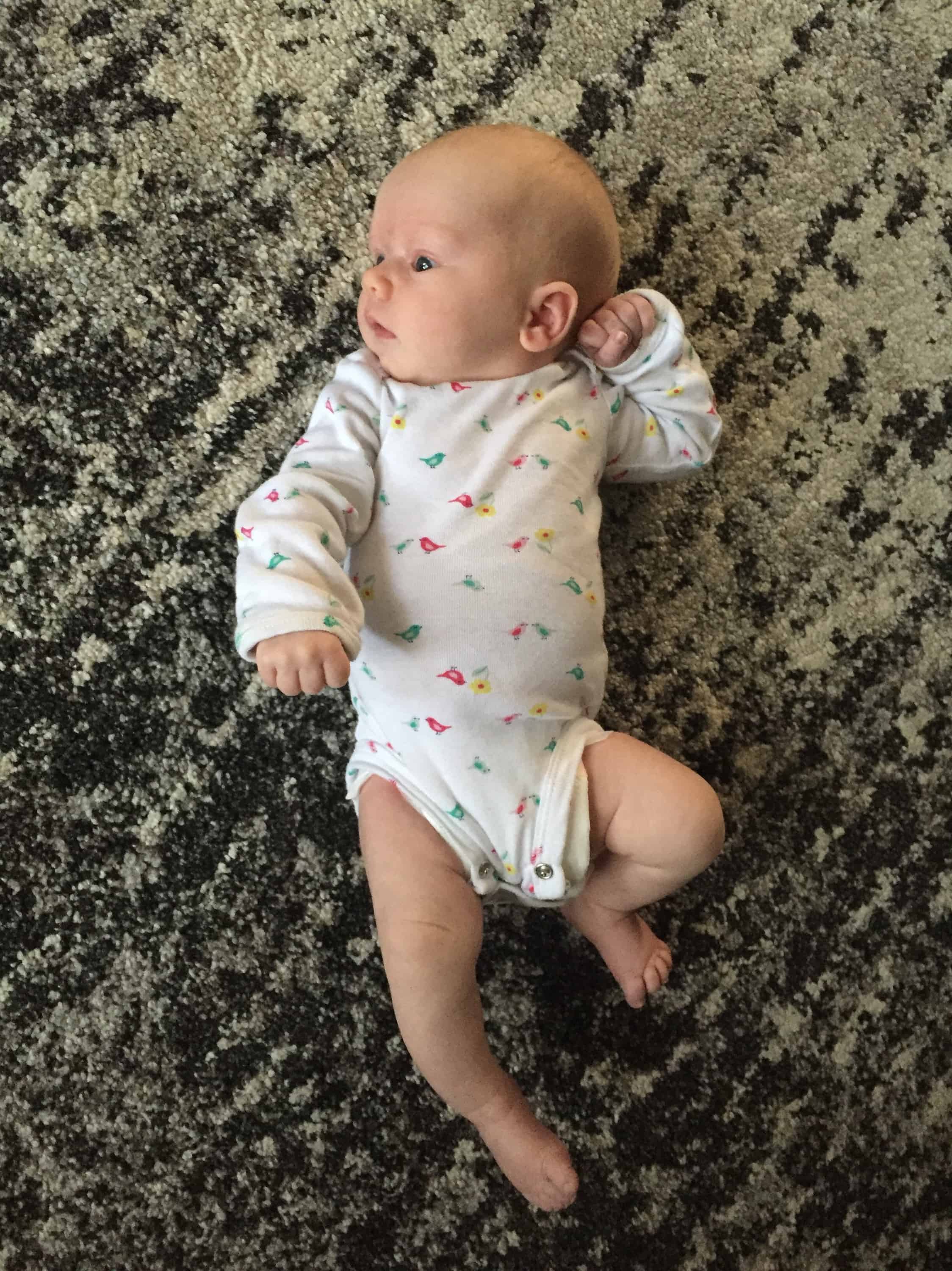 small baby in onesie laying on carpet