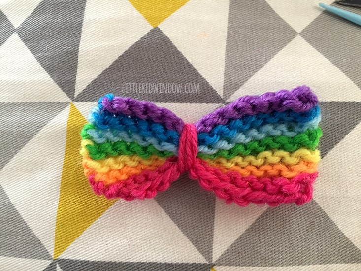 rainbow striped knit bow with a piece or pink string wound around just left of center