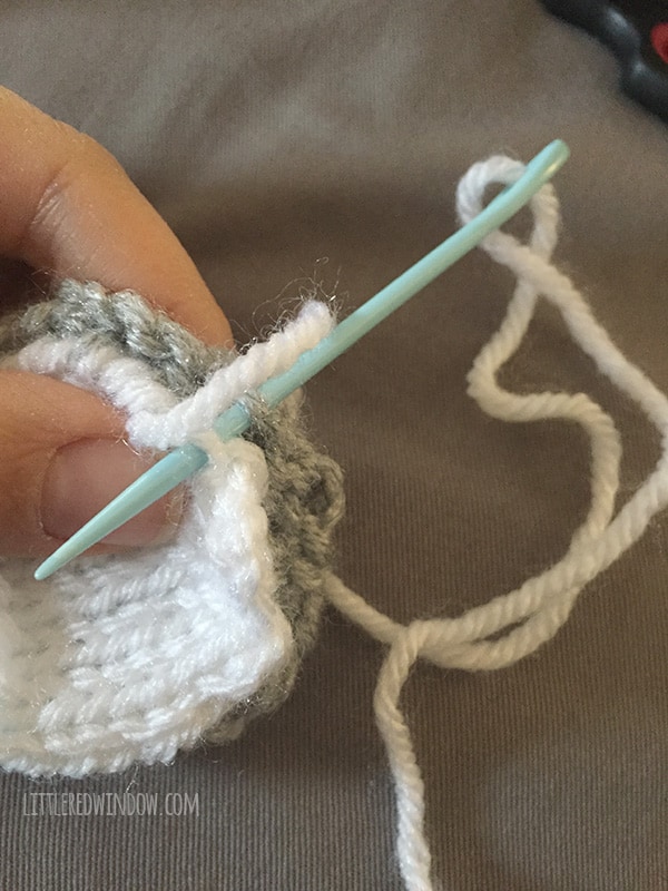Hand holding knit koala ears and sewing them together with blue yarn needle