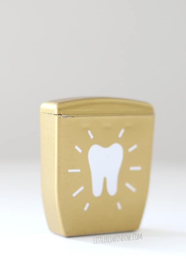 back view of gold dental floss container with white tooth shape in the center