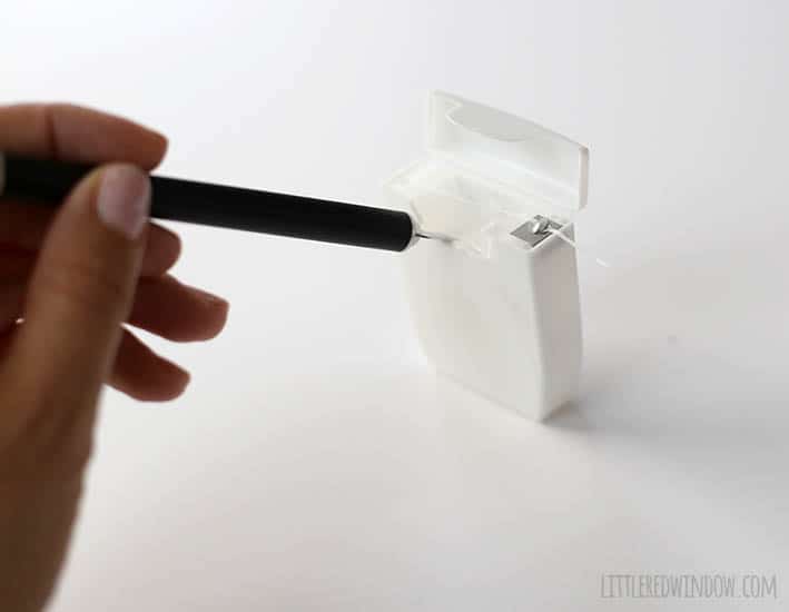 hand using craft knife to pop out the floss from inside a dental floss container