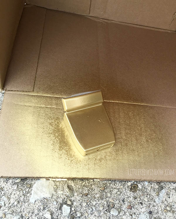 dental floss container spray painted gold on top of a piece of cardboard