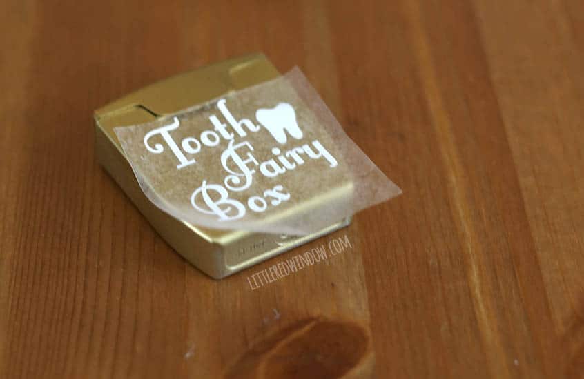 white vinyl label that says tooth fairy box being applied to the front of a gold dental floss container