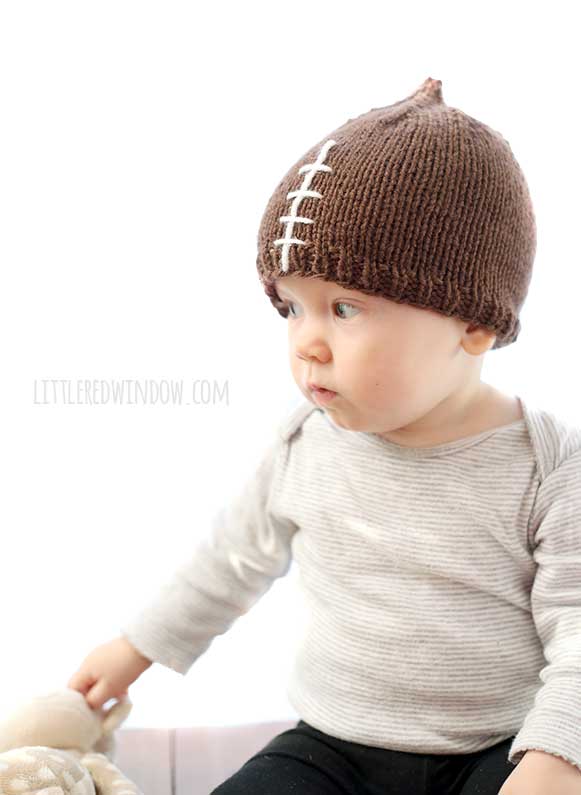 skeptical baby wearing gray shirt and brown knit hat that looks like a foodball