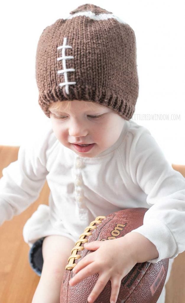 baby in football hat holding real football and leaning forward towards the camera