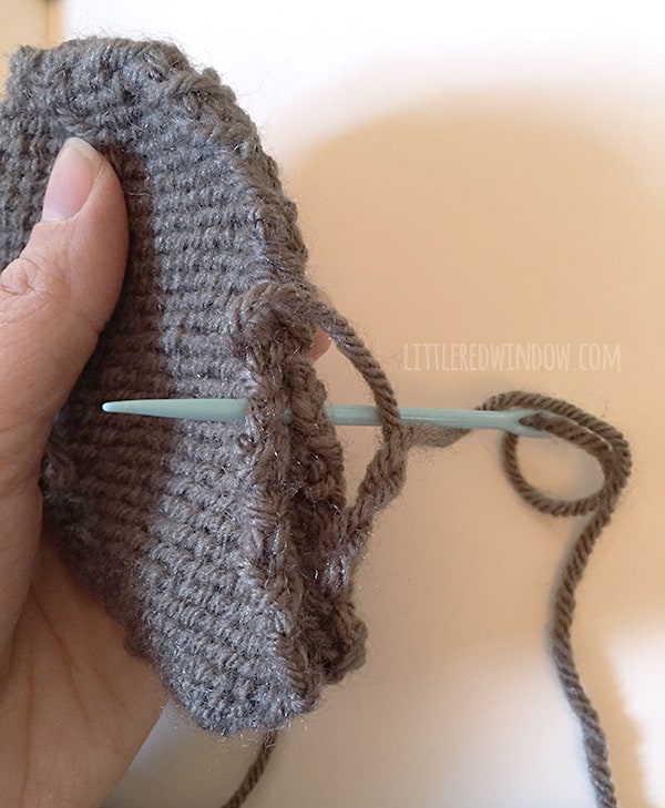 closeup of person stitches two ear halves wrong side together with a blue yarn needle 