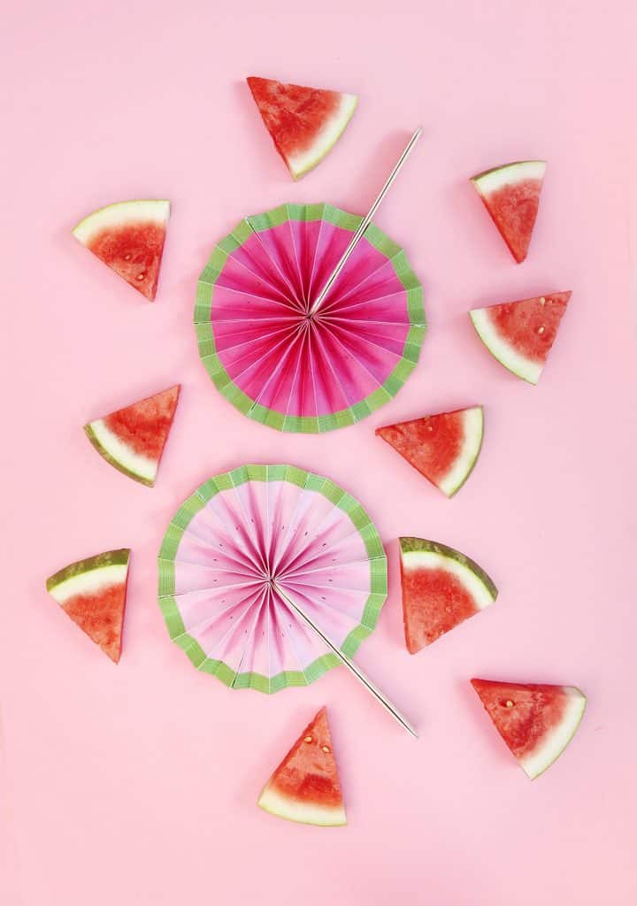 round watermelon colored folded paper fans with stick handles surrounded by slices of real watermelon