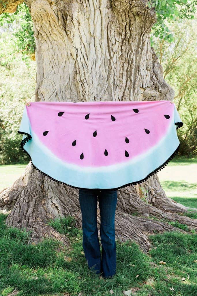 Person standing in front a of a tree and holding up a half circle blanked that looks like a wedge of watermelon