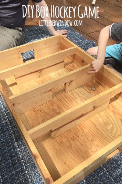 child flipping a bottlecap inside a wood box hockey stadium outside