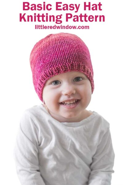 front view of smiling toddler in a white long sleeved tshirt in front of a white background wearing a basic knit hat with ribbed brim in ombre shades of raspberry and pink worsted weight yarn