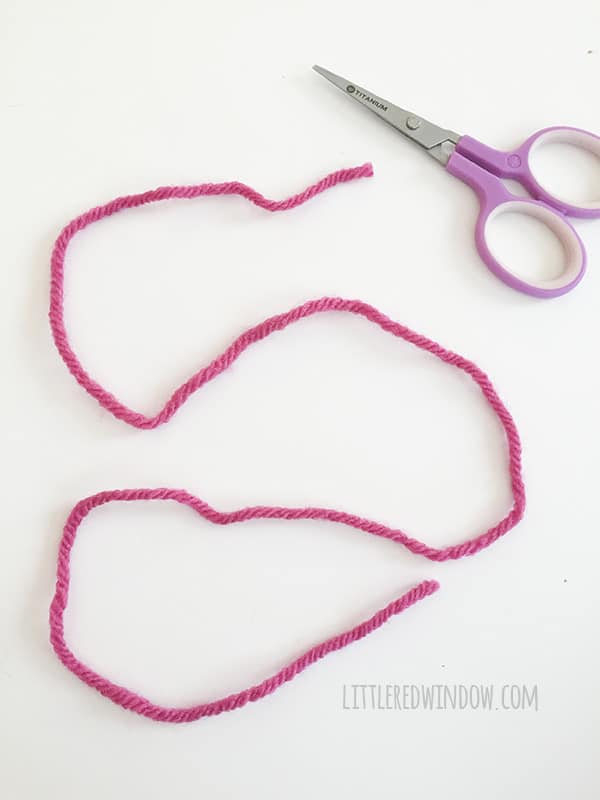 a pair of small purple scissors and length of hot pink yarn on a white background