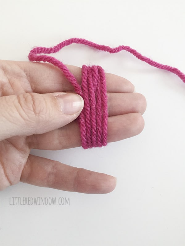 A hand with pink yarn wound around three fingers