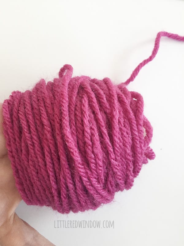 A hand with a lot of pink yarn wound around three fingers