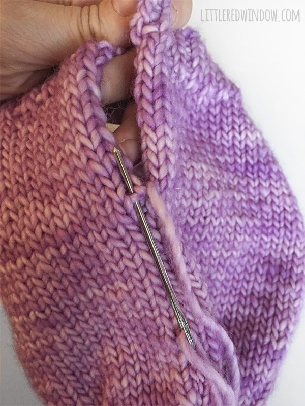 Hand holding the hat and using a yarn needle to demonstrate the Easy Knit Flat Baby Hat Seam technique
