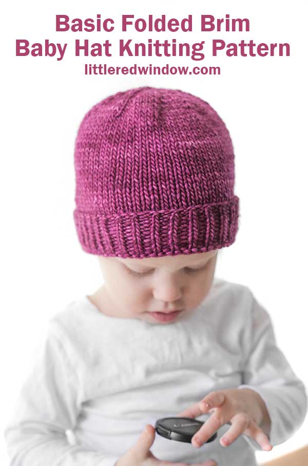 Girl in white shirt wearing a magenta knit hat with folded ribbed brim looking at something in her hands