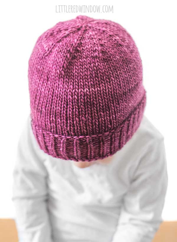 Top view of Girl in white shirt wearing a magenta knit hat with folded ribbed brim looking at something in her hands