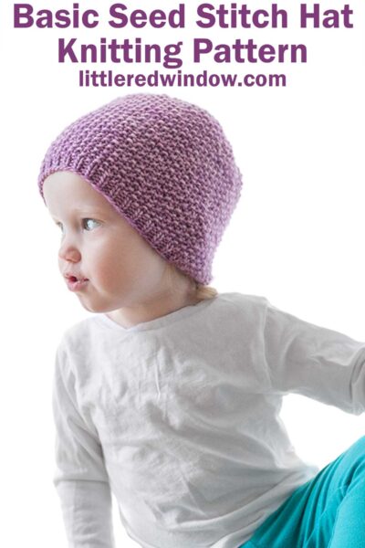 toddler in white shirt and teal pants leaning off to the left and wearing an orchid purple knit hat with small ribbed brim an the rest knit in seed stitch knitting pattern