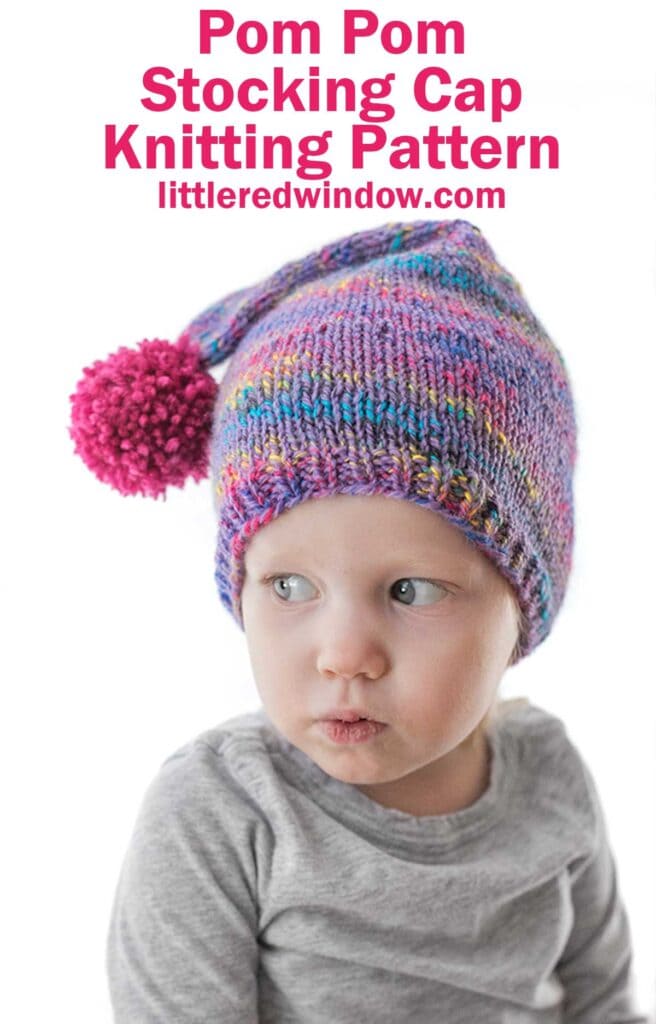 child in gray shirt with pursed lips wearing a purple speckled knit stocking cap with magenta pom pom hanging to the side while they look to the left 