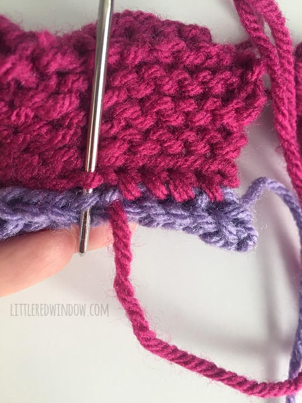Closeup of person sewing the pink wings of a knit butterfly to the purple body