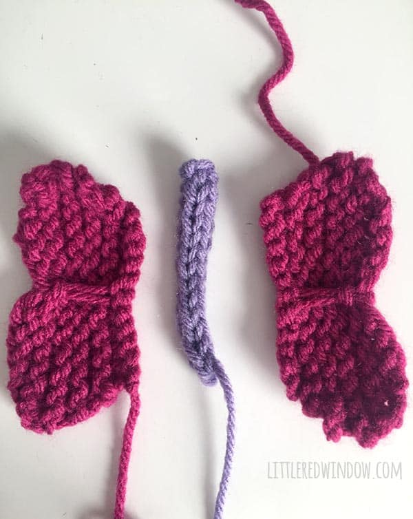 finished knit pieces of a butterfly laid out on a white tabletop pink wings and purple body