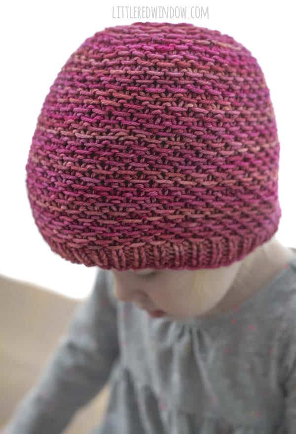 Little girl wearing magenta knit hat and looking down and to the left 