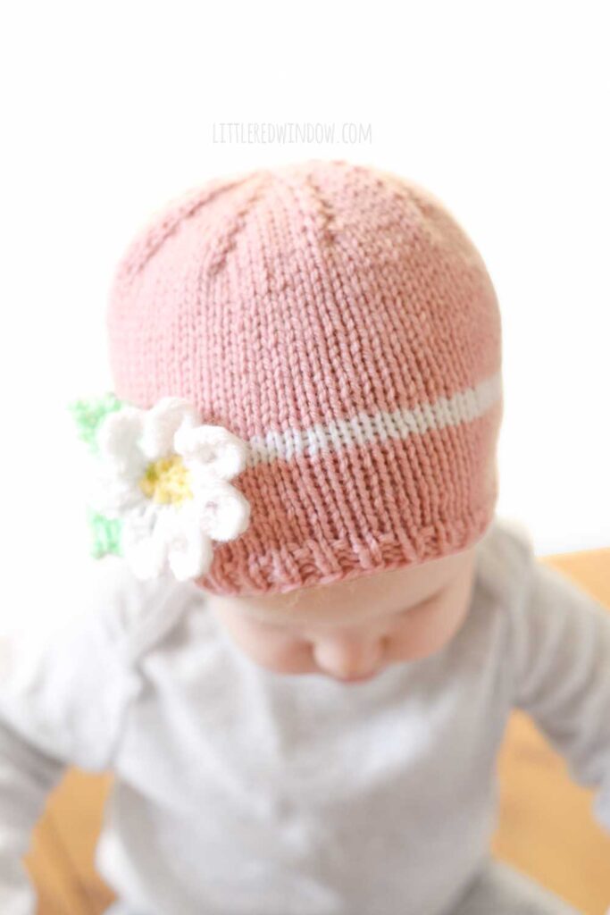 closeup of light pink knit spring daisy flower hat knitting pattern on a baby