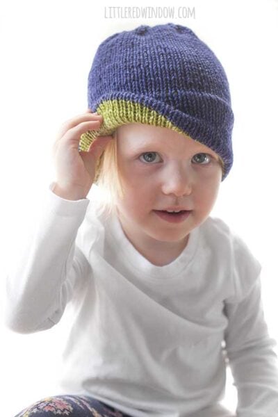 child wearing white shirt lifting up the brim of their navy blue knit hat to reveal lime green inside