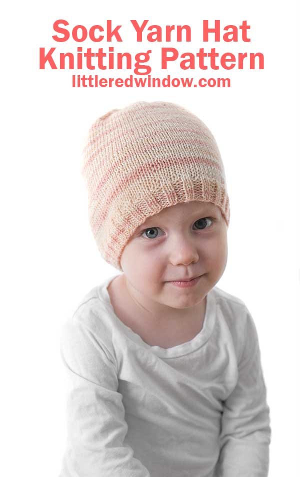 smirking baby looking at the camera and wearing a light pink sock weight yarn knit hat 