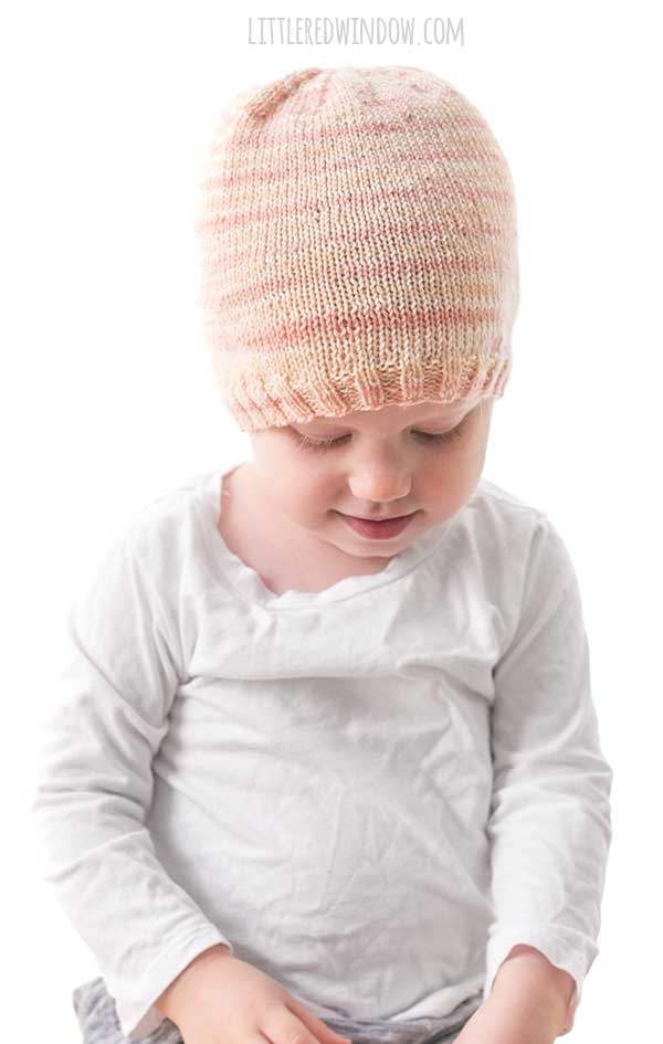 baby in white shirt looking down at their lap while wearing light pink self-striping sock weight yarn knit hat