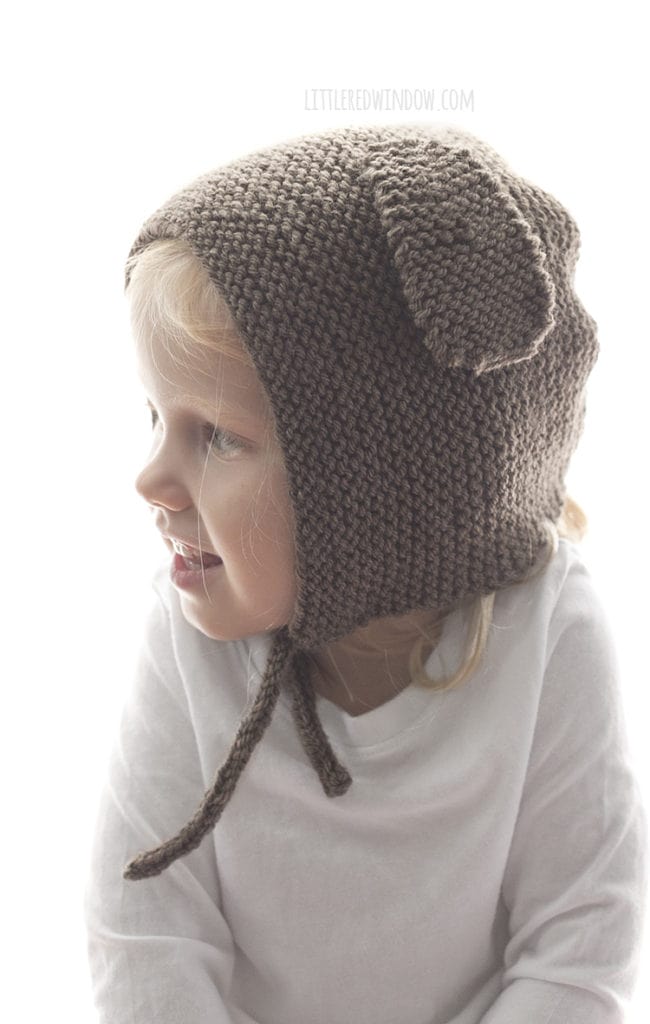 Little girl wearing brown knit bonnet with floppy puppy ears on the sides and looking to the left