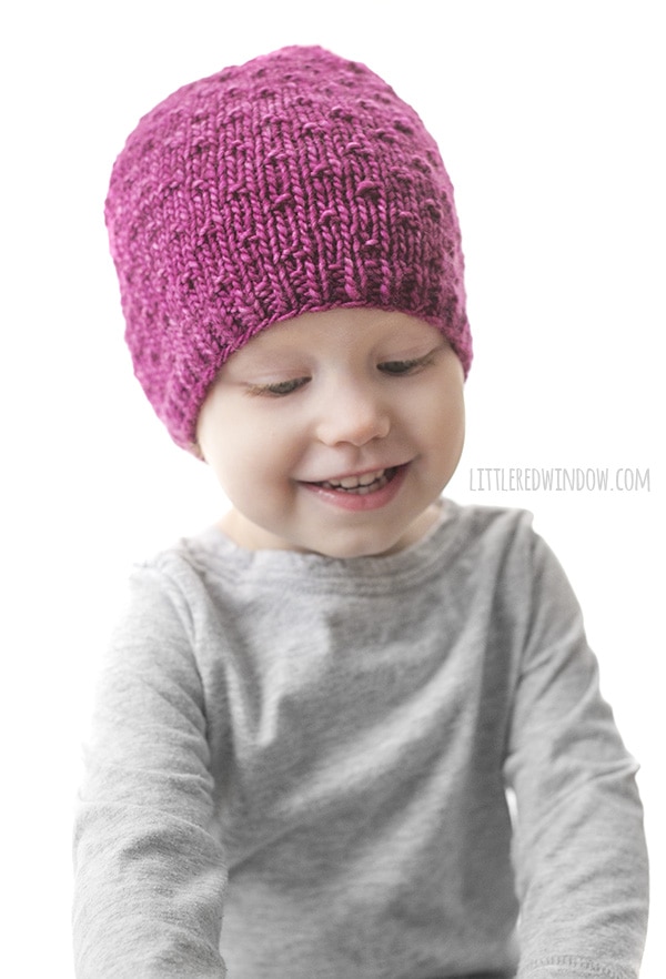 Smiling toddler wearing pink knit hat with polka dot texture
