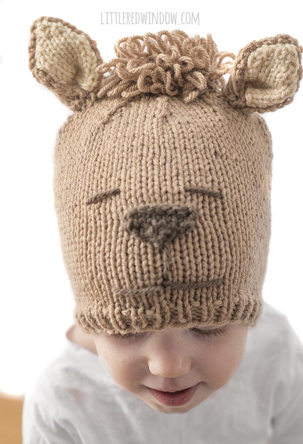 little girl looking down and wearing tan alpaca hat with brown nose and curly hair on top