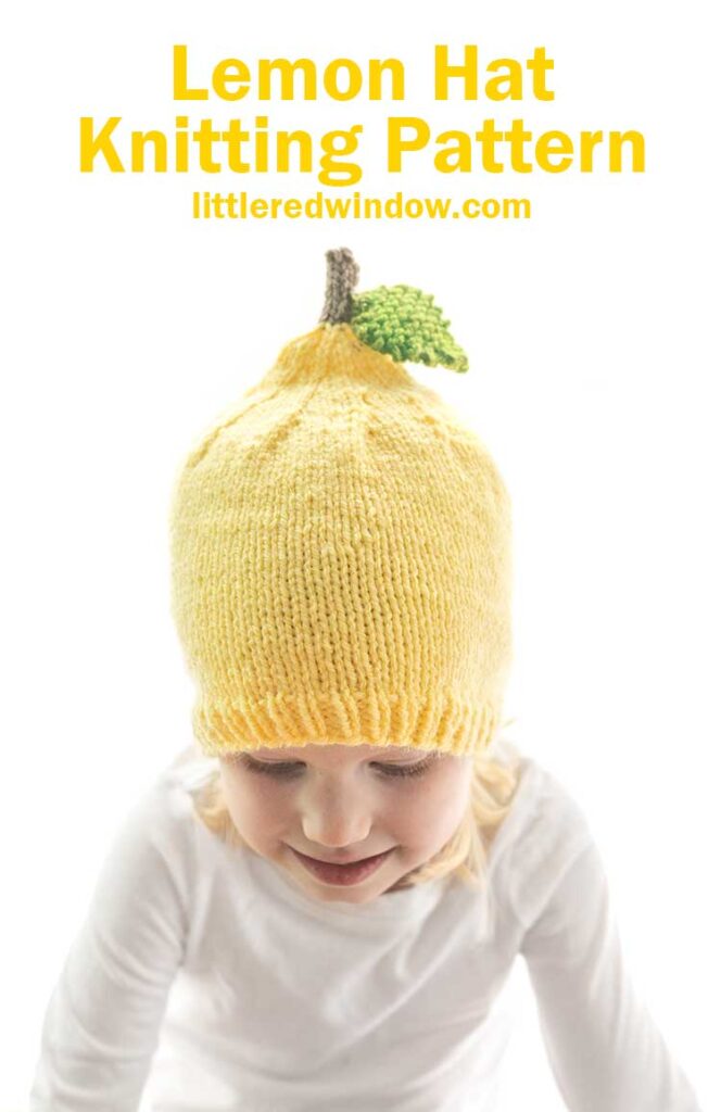 little girl in white shirt wearing yellow lemon knit hat with stem and leaf and looking down at the table